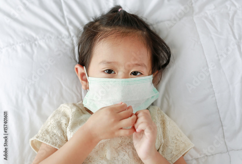 Asian little girl wearing a protective mask lying on the bed.