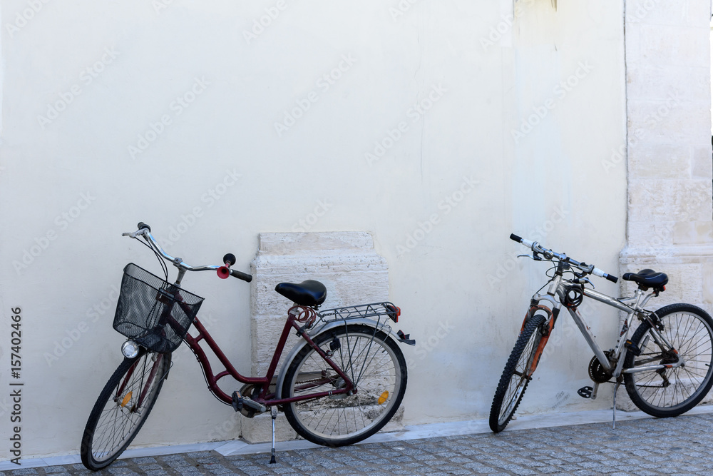 Two bicycles stand at a white wall