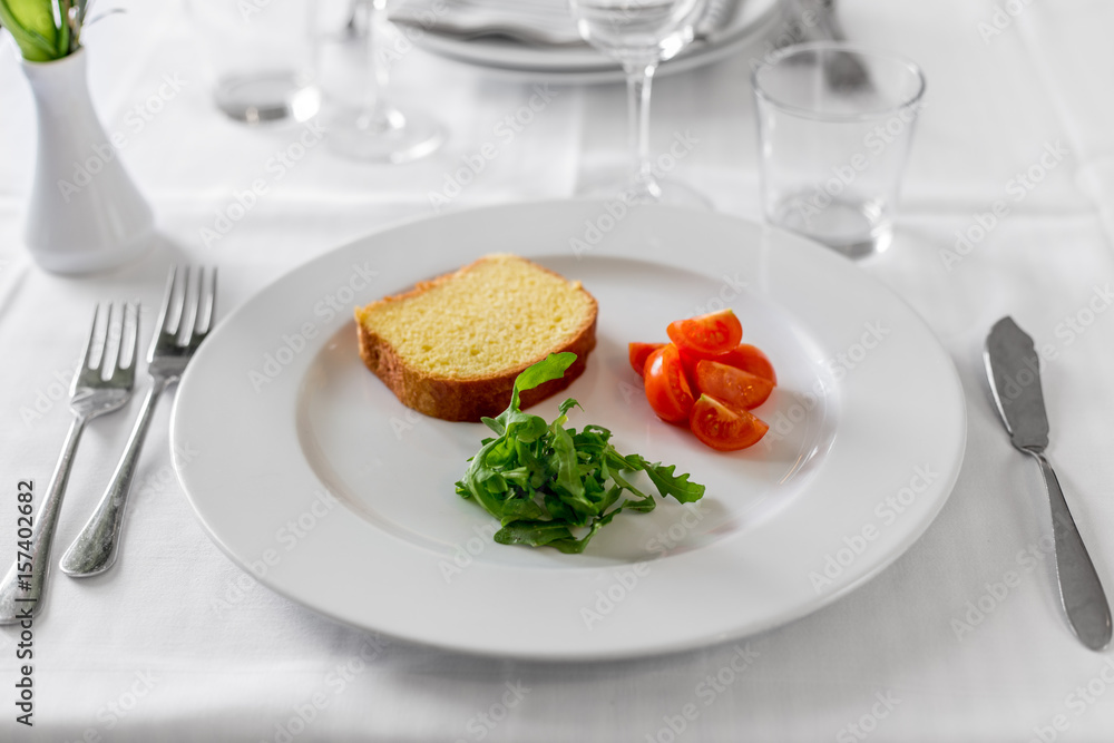 Restaurant table set with slice bread, cherry tomatoes, arugula.
