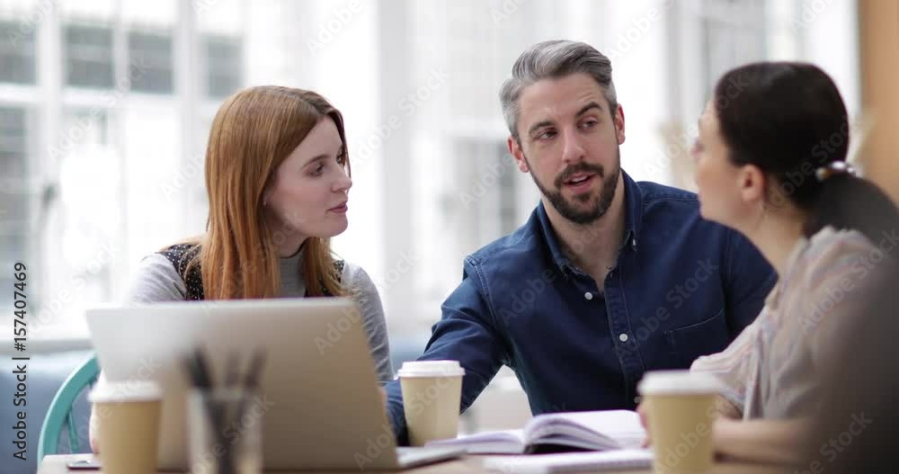 Coworkers looking at a laptop in a meeting Coworkers looking at a laptop in a meeting