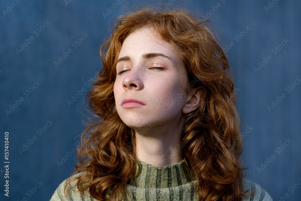 A red, beautiful girl with freckles closes her eyes and looks away. She enjoys the sun's warmth and light. A red, beautiful girl with freckles closes her eyes and looks away. She enjoys the sun's warmth and light.