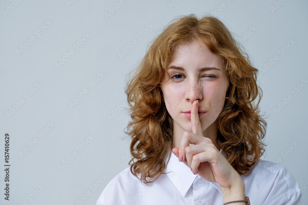 A red-haired, curly-haired girl with freckles puts her finger to her lips. A sign of silence or secret. A red-haired, curly-haired girl with freckles puts her finger to her lips. A sign of silence or secret.