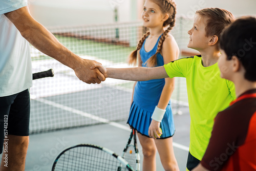 Proud tennis coach praising kid by handshake