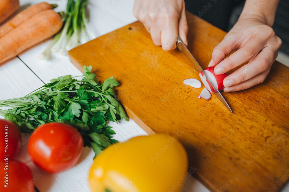 Woman hands cutting fresh red organic radish on wooden board closeup. White table background. Woman hands cutting fresh red organic radish on wooden board closeup. White table background.