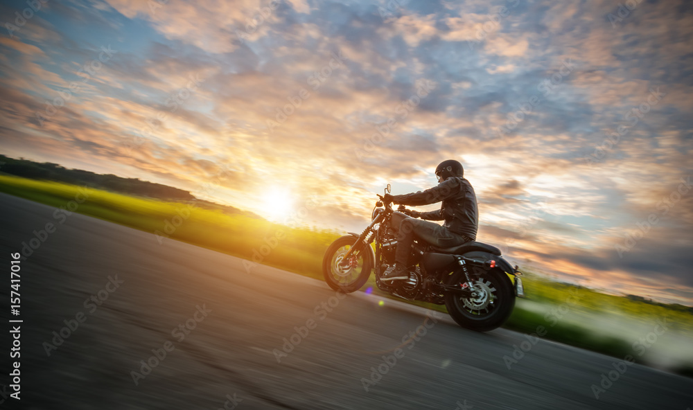 Fototapeta premium Ciemny motorbiker jedzie motocykl dużej mocy w zachodzie słońca