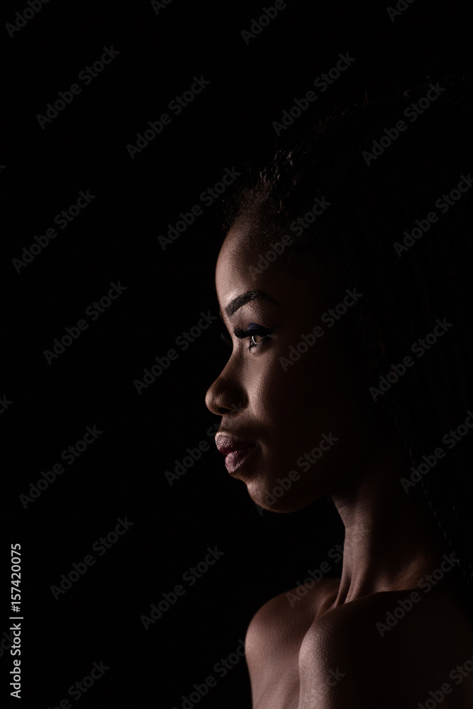 Black and white portrait of dark skinned model. Side view portrait of dark skinned woman on black backstage.