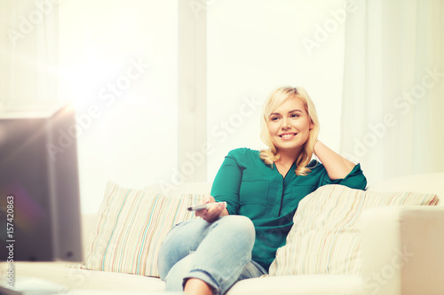 smiling woman with remote watching tv at home