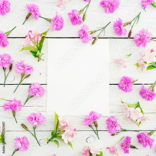 Floral pattern of pink flowers and paper card on white rustic background. Flat lay, top view. Floral concept