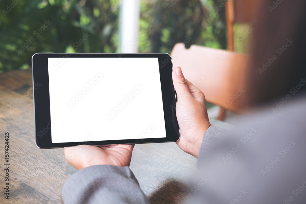 Mock up image of business woman's hands holding black tablet with white blank screen in cafe with nature background