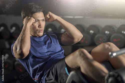 Asian man doing sit-ups at gym.