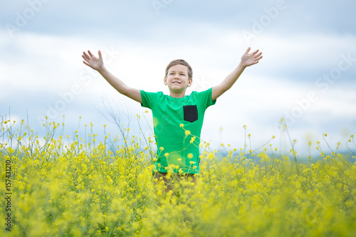 Happy cute handsome little kid boy on green grass lawn with blooming yellow dandelion flowers on sunny spring or summer day. Little boy dreaming and relaxing collecting a bouquet