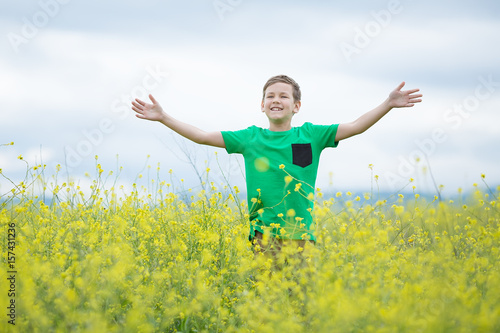 Happy cute handsome little kid boy on green grass lawn with blooming yellow dandelion flowers on sunny spring or summer day. Little boy dreaming and relaxing collecting a bouquet