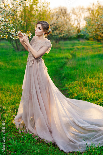 A girl in a long beige dress posing in the garden of blooming trees