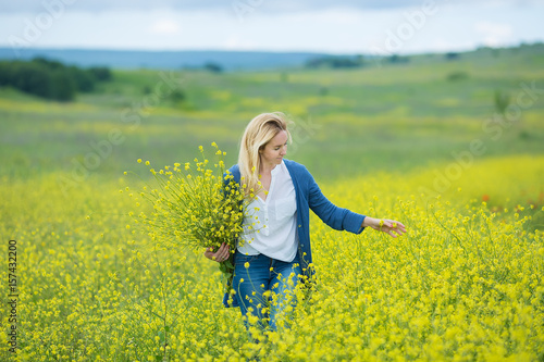 Genuine cute lady woman in meadow of yellow flowers sniffing flower bouquet. Attractive beautiful young girl enjoying the warm summer sun in a wide green and yellow meadow. Stylish dressed © TwinkleStudio