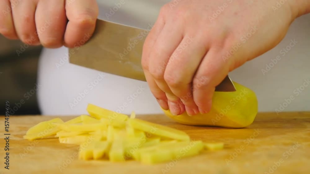 Side view woman cook cuts potatoes into slices on a wooden cutting board Side view woman cook cuts potatoes into slices on a wooden cutting board