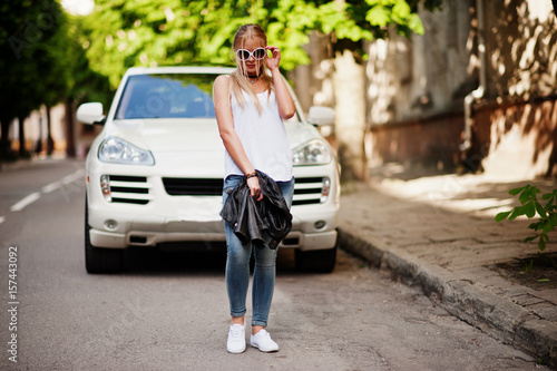 Stylish blonde woman wear at jeans, sunglasses, choker and white shirt against luxury car. Fashion urban model portrait. © AS Photo Family