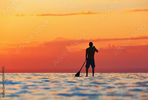 Paddle boarder. Black sunset silhouette of young sportsman paddling on stand up paddleboard. Healthy lifestyle. Water sport, SUP surfing tour in adventure camp on active family summer beach vacation.