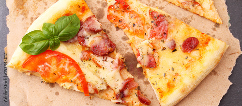 Pizza with sausage, ham, tomato and cheese, decorated with basil and cut into pieces on a parchment