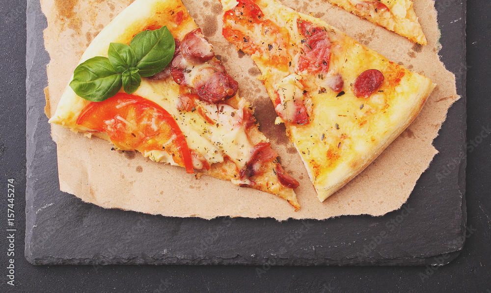 Pizza with sausage, ham, tomato and cheese, decorated with basil and cut into pieces on a parchment Pizza with sausage, ham, tomato and cheese, decorated with basil and cut into pieces on a parchment