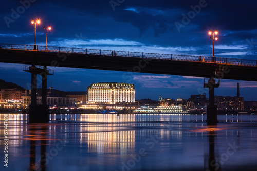 Night european city in colorful lights and reflection in water, Kyiv (Kiev) the capital of Ukraine. Pedestrian bridge across the Dnieper river and view to the river station