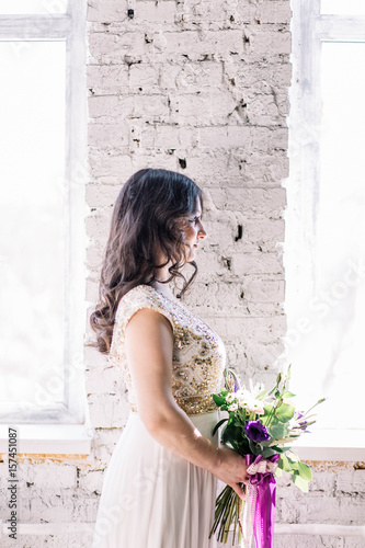 beautiful sexy Oriental girl brunette bride in white wedding dress with Golden sequins, a bouquet on a brick background in Studio near the window profile © liliyabatyrova