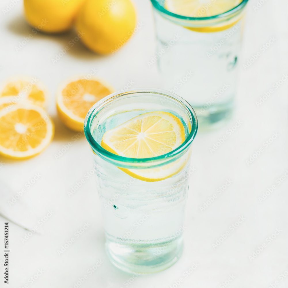 Morning detox lemon water in glasses served with fresh lemons over light grey marble background, selective focus, square crop. Clean eating, weight loss, healthy, detox, dieting concept Morning detox lemon water in glasses served with fresh lemons over light grey marble background, selective focus, square crop. Clean eating, weight loss, healthy, detox, dieting concept