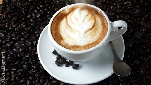 Hot cappuccino or latte art. A cup of coffee on the wooden table with roasted coffee beans. Morning breakfast. The shape created by pouring steamed milk.