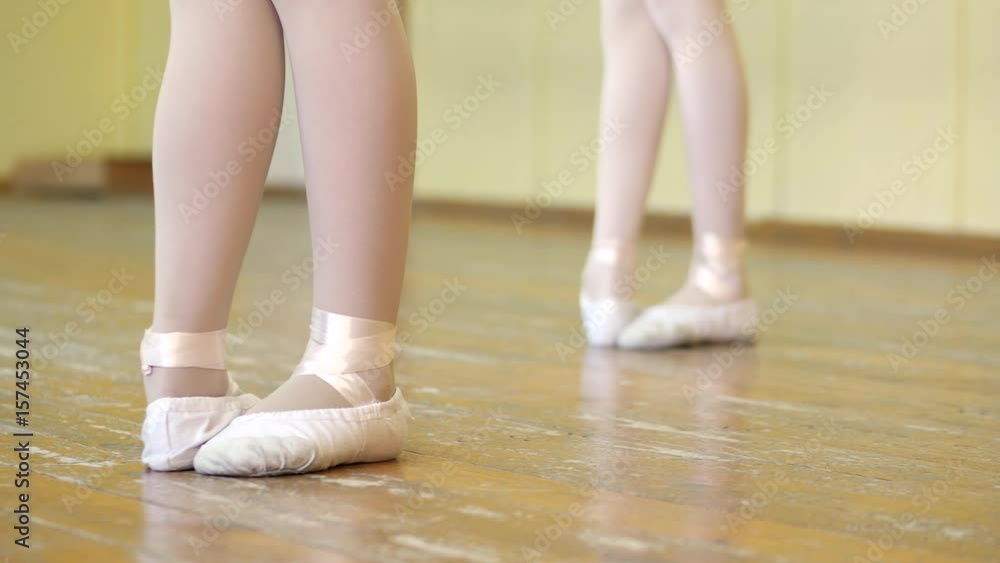 Close-up of a girl's legs in white ballet shoes on an old wooden floor during ballet training. Element of classical dance exercise. Close-up of a girl's legs in white ballet shoes on an old wooden floor during ballet training. Element of classical dance exercise.