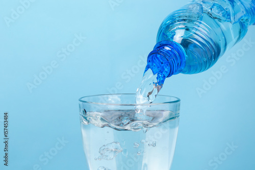 Water pouring from bottle into glass on color background