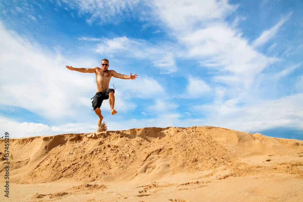 Happy and cheerful guy jumping on the beach against a beautiful blue sky with clouds Happy and cheerful guy jumping on the beach against a beautiful blue sky with clouds