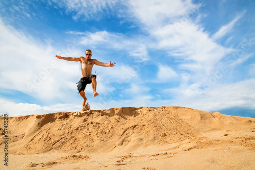 Happy and cheerful guy jumping on the beach against a beautiful blue sky with clouds