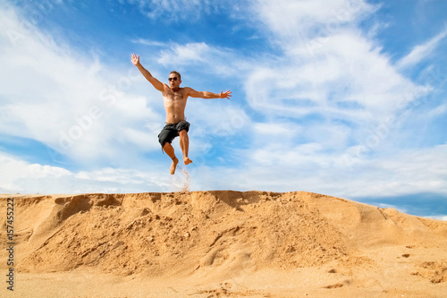 Happy and cheerful guy jumping on the beach against a beautiful blue sky with clouds