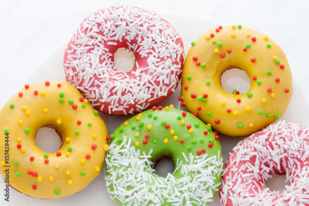 Yellow, green and pink Donuts with polka dots on a plate on a white background. National Doughnut Day. Dessert food. Fried dough confectionery. Snacks. Yellow, green and pink Donuts with polka dots on a plate on a white background. National Doughnut Day. Dessert food. Fried dough confectionery. Snacks.