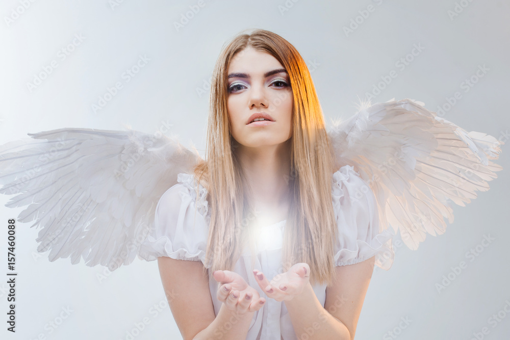 An angel from heaven holding something on the palms. Young, wonderful blonde girl in the image of an angel with white wings. An angel from heaven holding something on the palms. Young, wonderful blonde girl in the image of an angel with white wings.