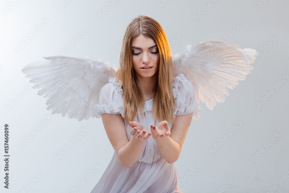 An angel from heaven holding something on the palms. Young, wonderful blonde girl in the image of an angel with white wings. An angel from heaven holding something on the palms. Young, wonderful blonde girl in the image of an angel with white wings.