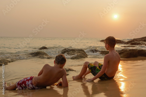 scenic beautiful romantic sunset over the sea with children sitting in water and enjoy the evening orange sun at adaman ocean, Surin Beach Phuket island, Thailand