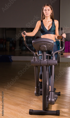 Attractive young woman is working out on an elliptical trainer in gym.