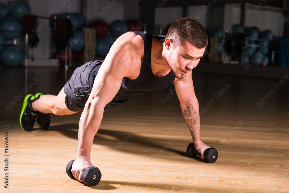 Gym man push-up strength pushup exercise with dumbbell in a fitness workout Gym man push-up strength pushup exercise with dumbbell in a fitness workout