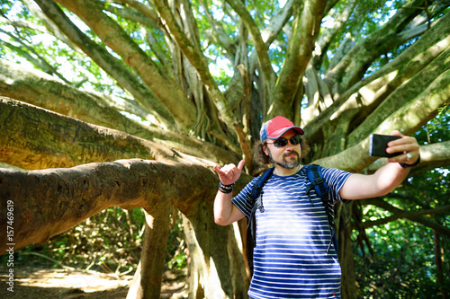 Male tourist taking photo of himself near giant banyan tree on Hawaii photo