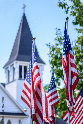 one nation under God - US flags standing outside old white church steeple in daylight