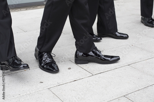 Feet and legs of male wedding party wearing black tuxedoes and black shiny shoes