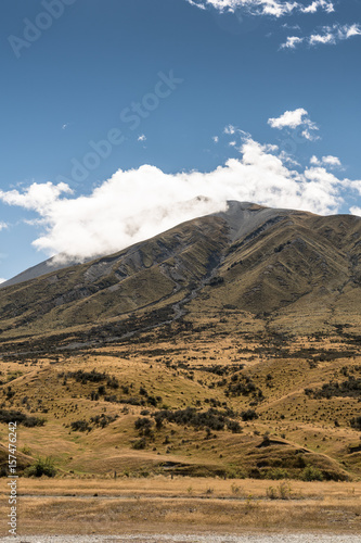 Middle Earth, New Zealand - March 14, 2017: Mountain at Middle Earth under blue cloudy sky. High desert scenery with sparse brown vegetation. Shale pebble flow off top.