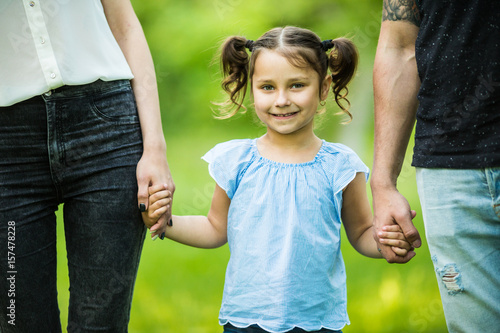 Excited young girl holding hands while walking with parents in summer park