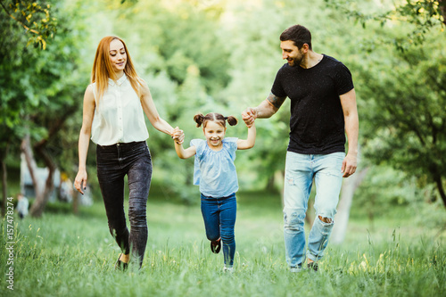 happy mother, father and little girl running together and have fun in summer park