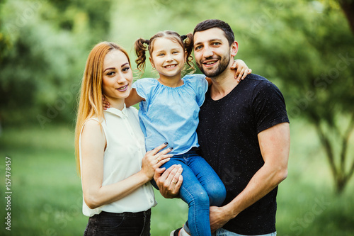 Happy young family spending time together in green nature. wife with husbend and daughter. Mother and father holding daughter in park © F8  \ Suport Ukraine