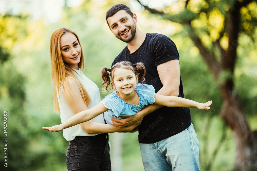 Fototapeta premium Happy young family play in summer park. Mother, father and daughter fly in the summer park.