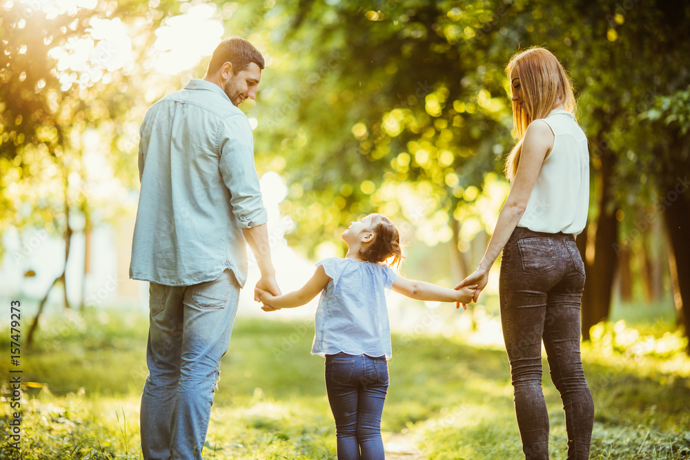 Happy family in the park. Mom, dad and baby happy walk at sunset. The concept of a happy family. Parents hold the baby's hands. Happy family in the park. Mom, dad and baby happy walk at sunset. The concept of a happy family. Parents hold the baby's hands.
