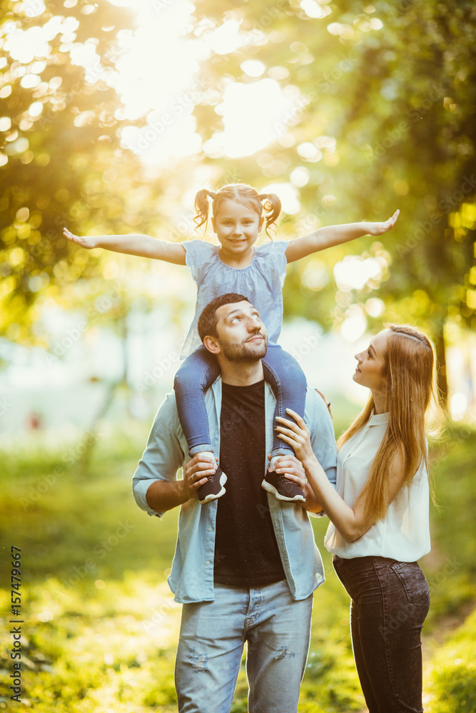 Fototapeta premium happy family Mom and Dad holding daughter on his back and have fun in the park.