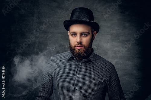 Bearded male smoking electronic cigarette over grey background.
