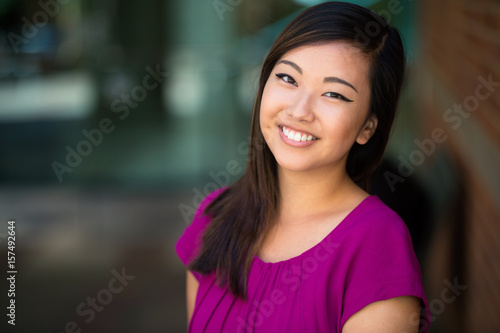 Cute pretty young youthful head shot of asian american woman with genuine natural smile bright colors